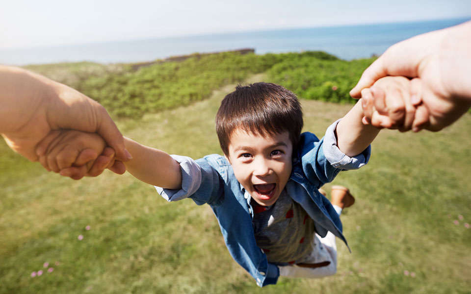 adult swinging happy child by the arms outside